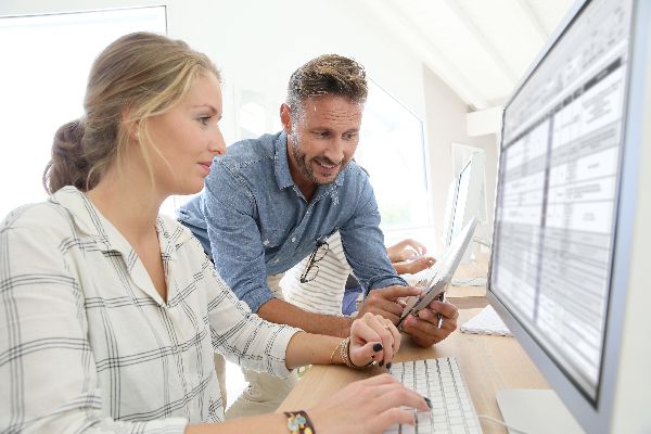 Foto de dos personas coversando y utilizando un ordenador